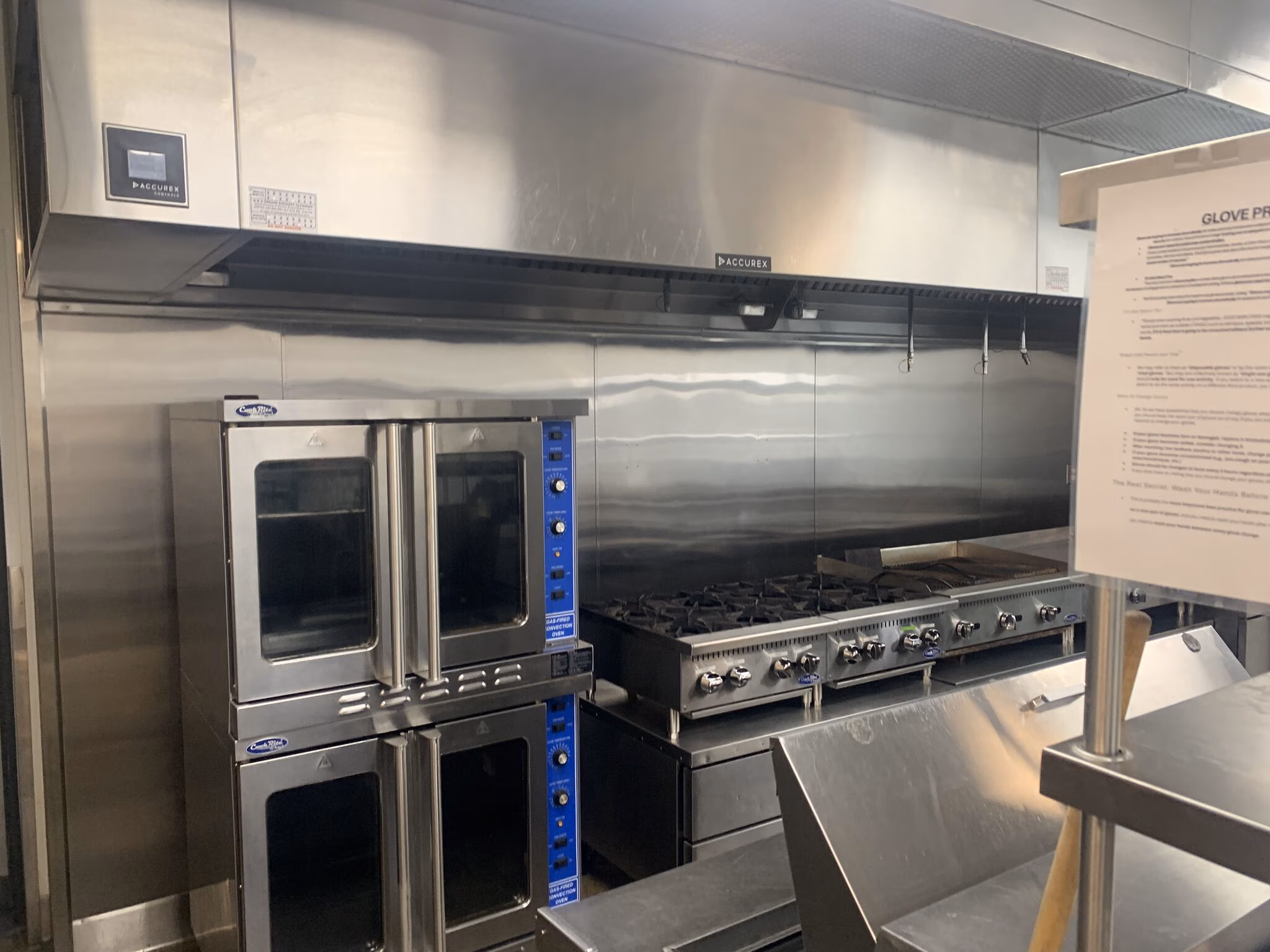 Commercial kitchen with a double convection oven, stovetop with burners, and stainless steel surfaces.