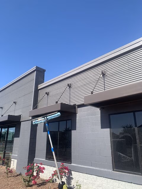 Building exterior with gray walls, large tinted windows, and a window cleaning tool resting on one window.