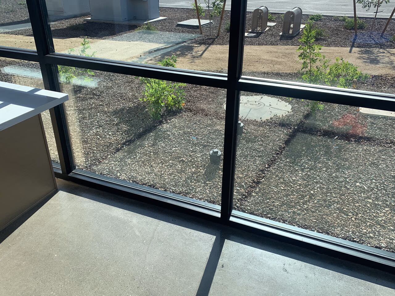 View through large window showing gravel ground, small plants, and a concrete floor inside.