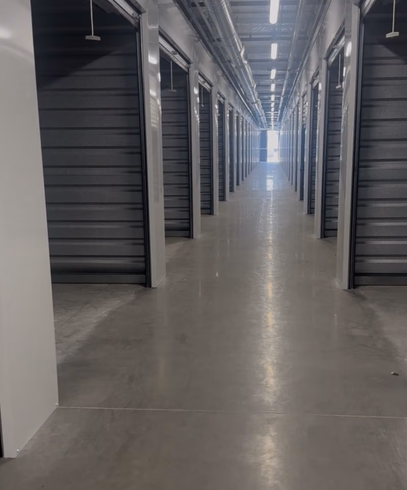 Long corridor lined with closed metal storage unit doors on both sides in a warehouse.
