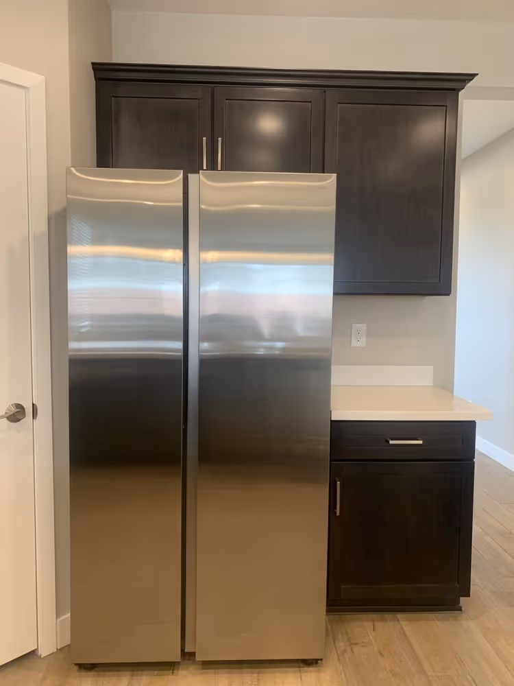 Stainless steel side-by-side refrigerator with dark wood cabinets and light countertop in kitchen.