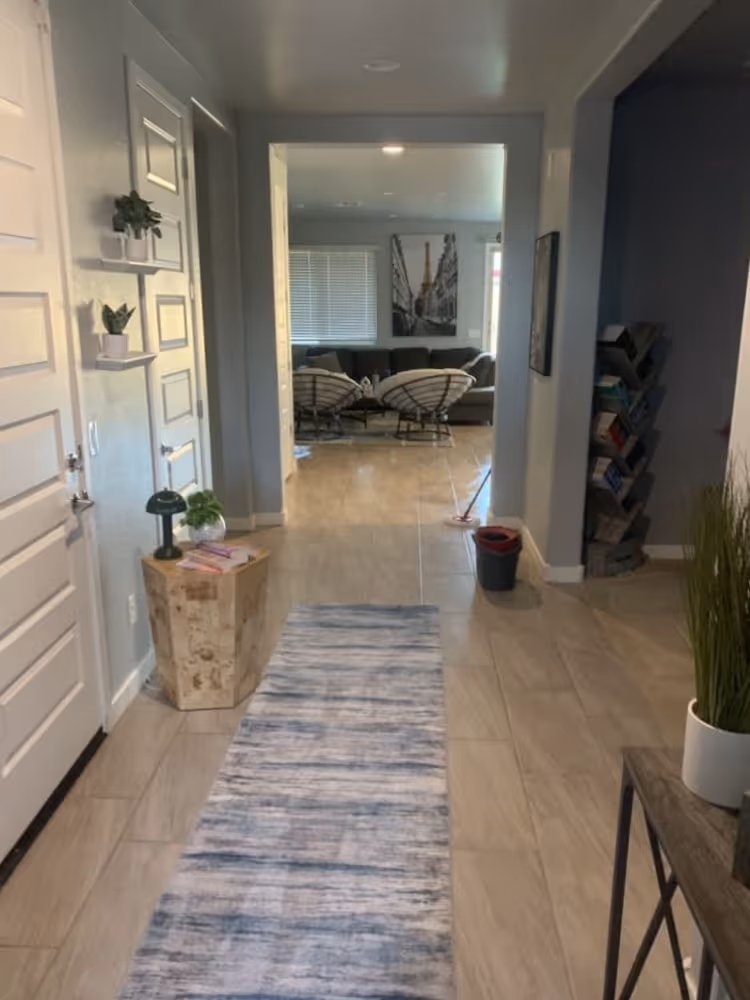 Hallway with blue runner rug leading to living room with chairs, couch, and Eiffel Tower wall art.