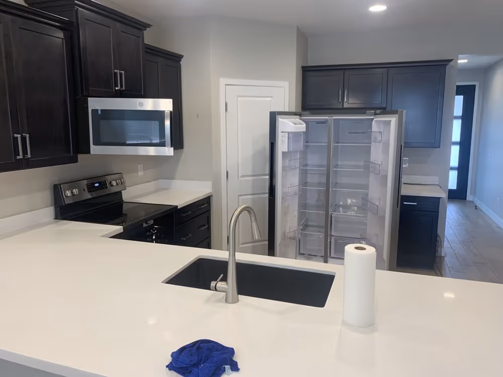 Modern kitchen with dark cabinets, stainless steel appliances, white countertop, and open fridge.