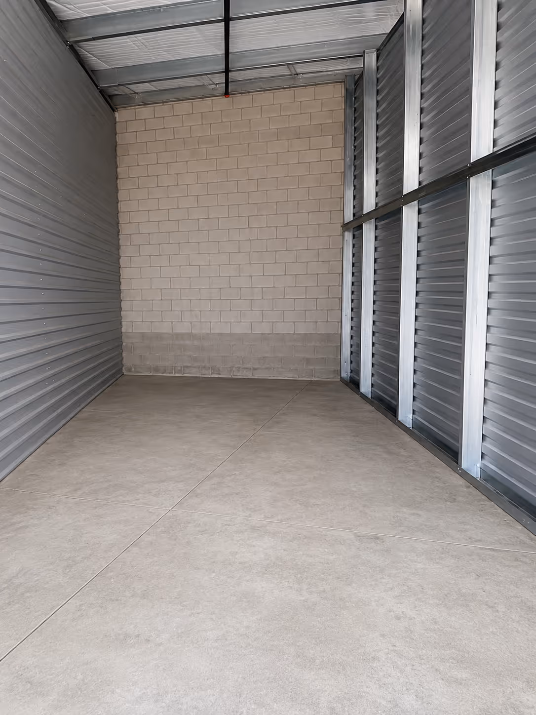 Empty storage unit with concrete floor, block wall, and corrugated metal walls and ceiling.