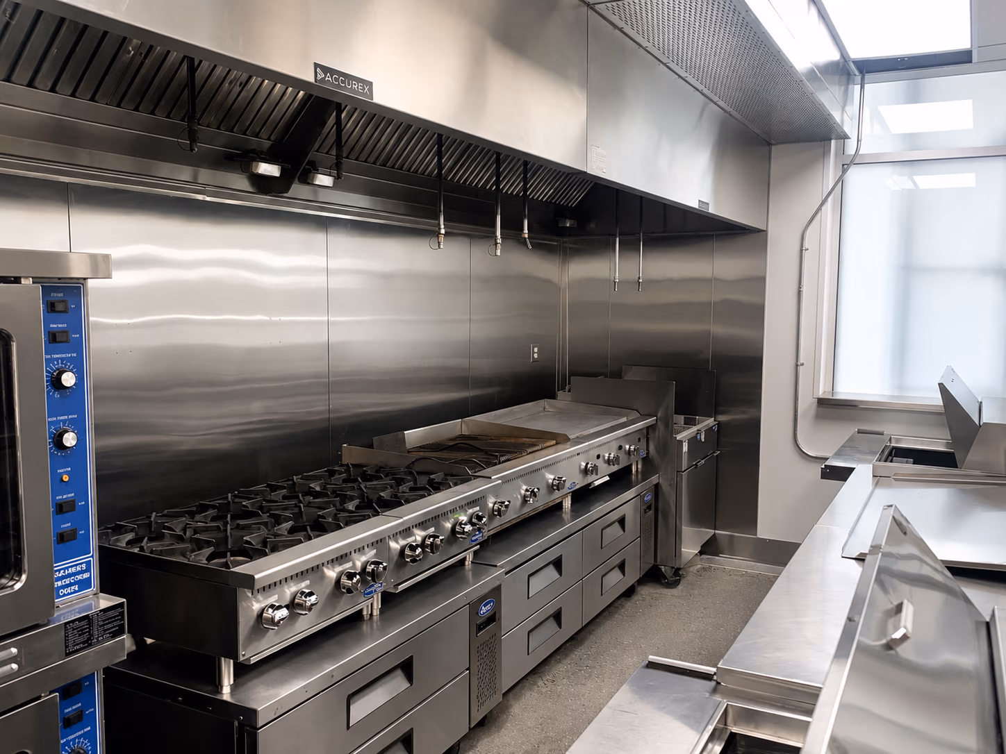 Clean commercial kitchen with large stainless steel stove, oven, fryer, and ventilation hood.