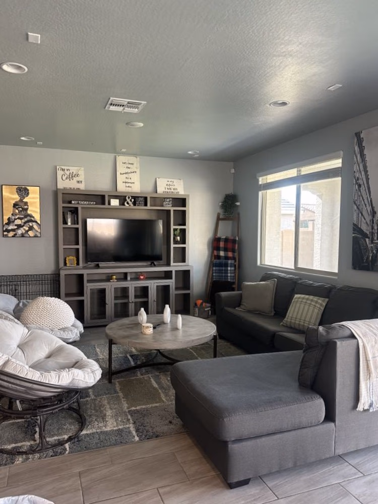 Cozy living room with gray sectional, round coffee table, papasan chair, and entertainment center with TV.