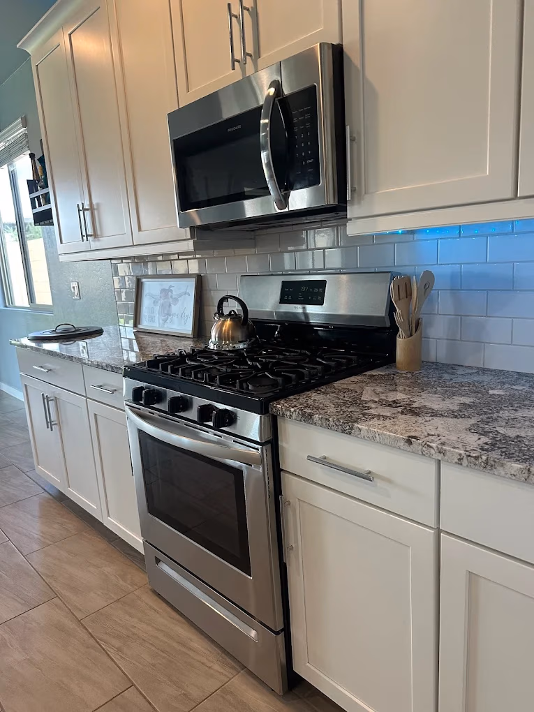 Modern kitchen with stainless steel stove and microwave, white cabinets, and granite countertops.