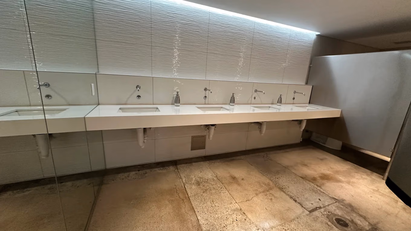 Modern public restroom sinks with soap dispensers and motion-activated faucets under soft ceiling lighting.