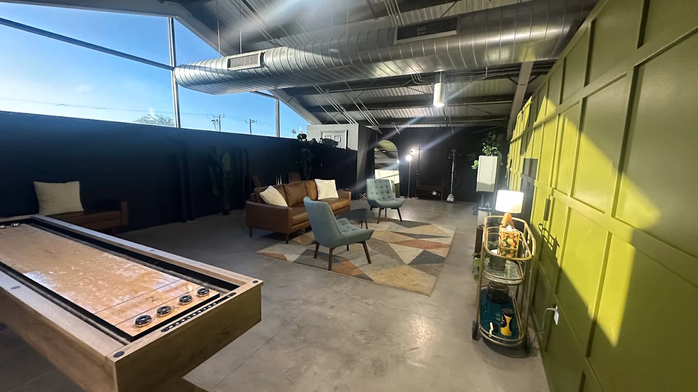 Modern lounge with leather sofa, blue chairs, patterned rug, shuffleboard, and green accent wall.