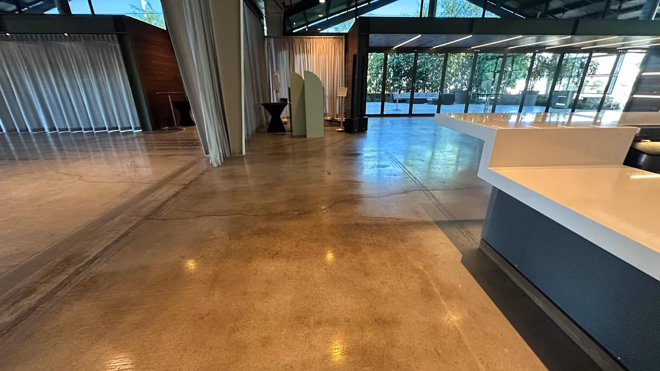 Empty modern event space with polished floor, white curtains, glass wall, and a white counter on the right.